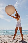 A woman on a beach doing yoga stretching with an exercise ball
