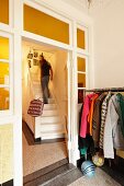 Coat rack next to lattice door in hallway and man walking up white wooden staircase in rustic stairwell