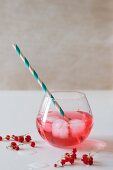 A glass of red fruit juice with ice cubes, redcurrants and a retro straw