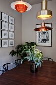 Various, retro-style pendant lamps above vase of flowers on dining table and classic chairs; framed pictures on wall
