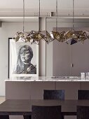 Designer pendant lamp above dark brown dining table and kitchen counter with marble worksurface; framed photographic portrait of woman