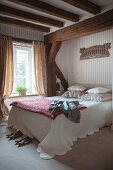Schlafzimmer mit Holzbalkendecke, drapierte Kissen und Tagesdecke auf Doppelbett, an Wand Tapete mit Streifenmuster