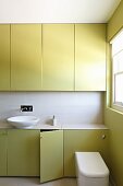 Green fitted cupboards and white countertop basin in bathroom