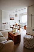 Lounge area with patterned pouffe next to coffee table and sofa; dining area next to window in background