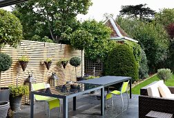 Elegant, grey outdoor tables and neon-green chairs on terrace in front of slatted wooden screen