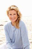 A blonde woman on a beach wearing a blue jumper