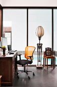 Desk with modern office chair, ethnic floor lamp in front of floor-to-ceiling glazing