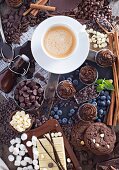 An arrangement of chocolate featuring cookies, cupcakes, chocolate chips, syrup, marshmallows, blueberries, cinnamon sticks and coffee
