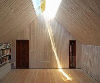 Wood-clad attic room with skylights along ridge and sunlight reflected onto wooden floor