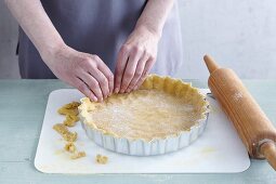 Gluten-free shortcrust pastry being pushed into a baking dish