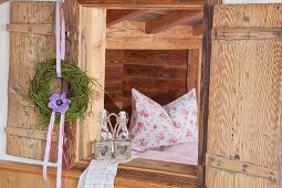 Wreath of bilberry stalks and anemone hung from open shutter and view of pillow on bed through open window