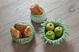 Apples and pastries in crocheted baskets on wooden surface