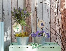 Gestickte Pflanzenstecker in bepflanzeten Zinktöpfen vor Vintage-Holzwand