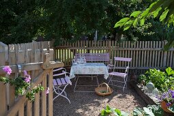 Romantische Sitzplatz vor Lattenzaun und Laubbäumen im Garten