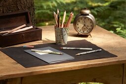 Pen holder covered in map and old alarm clock on wooden table outdoors