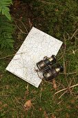 Old pair of binoculars and map on mossy ground