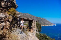 A woman practising yoga by a rustic stone house above a bay