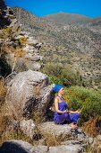 Frau in violettem Ensemble und Turban meditiert an Felsen
