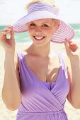 A young woman wearing a purple beach dress and a sun hat by the sea