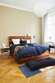 Elegant wooden bed with blue bed linen in bedroom with herringbone parquet floor