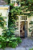 Ferns and climbing plants outside traditional house with open door