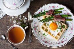A savoury waffle with a fried egg, asparagus wrapped in ham and chives