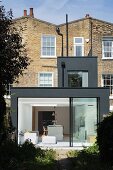 Modern, dark grey extension to Georgian terrace house with open sliding glass wall leading to garden