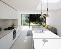 weiße Designerküche mit Küchentheke und Lichteinstrahlung durch Oberlicht, offener Blick in den sommerlichen Garten