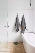 Freistehende Badewanne in bodenebenem Duschbereich mit schwarz-weiß gestreiften Handtüchern an weiß gefliester Wand