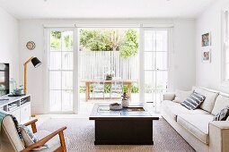 Living room with box-shaped coffee table and light sofa in front of open patio doors and view of the outdoor dining area