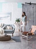 Runder Polstertisch auf Webteppich, Sofa und skandinavischer Sessel mit Ledersitz, Frau vor Wand mit Tapetenbahnen