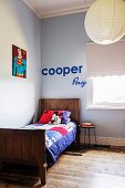 Bunte Patchworkdecke auf Holzbett in hellblauer Zimmerecke, an Wand 'Superman' Bild und Deko-Buchstaben