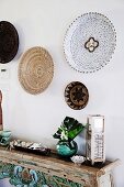 Carved ethno console table with decorative objects and wicker plates on the wall
