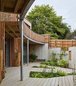 Modern, shared, eco-home with encircling balcony and wooden deck with recessed beds of plants