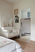 White couch against protruding section of wall and rustic door leading to ensuite bathroom