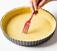 Shortcrust pastry being pierced with a fork for blind baking