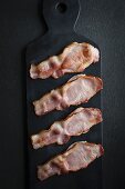 Four rashers of bacon on a black slate platter