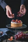 Frauenhände verzieren selbstgemachte Torte mit roten Trauben, Feigen und Schlagsahne