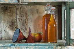 Bottles of apple juice, a funnel and Jonagold apples on a rustic shelf