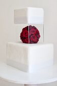 Zweistöckige Hochzeitstorte mit Plexiglasständer und roter Rosendeko