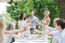 Family garden party: a family raising a toast to a young couple with a baby