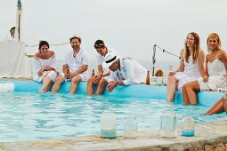 Wedding guests in summer clothes sitting by the side of a pool