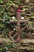 Rusty anchor, metal cross and ornaments against stone wall in garden