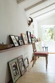 Antique upholstered chair below shelf of pictures and pictures on floor leaning against wall