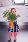 A little girl holding a large bundle of carrots