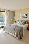 Grey bedspread on double bed next to terrace windows in modern bedroom with pale grey resin floor