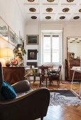 Stucco ceiling roses, brown leather armchair and dining area with antique chairs around classic Tulip Table below window