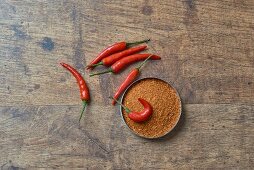 Chilli powder and fresh chillis on a wooden surface (seen from above)