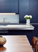 Blaugraue Designerküche mit Küchentheke, indirekter Beleuchtung und Edelholztisch