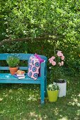 Crocheted cushions on blue-painted garden bench next to pink potted rose
